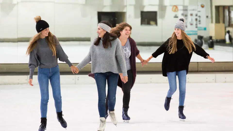 Vier Eisläuferinnen halten sich auf der Eisfläche an den Händen