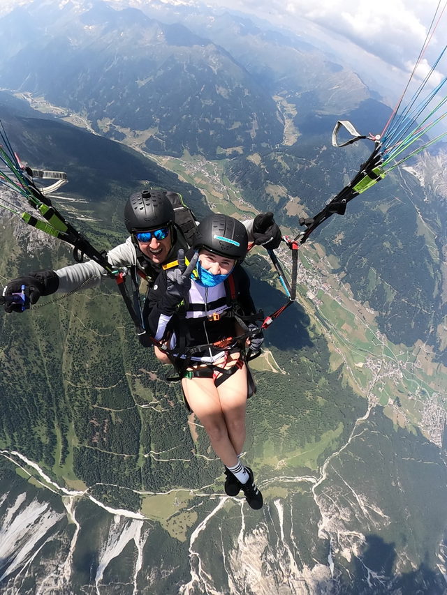 Pilot und lächelnder Fluggast beim Paragliding über einem alpinen Tal