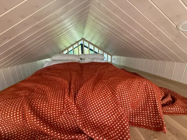 Schlafempore im Dachgeschoss aus Holz mit rotem gepunktetem Deckenbezug.