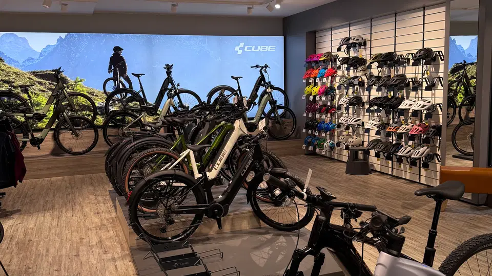 Innenansicht eines Fahrradgeschäfts mit E-Bikes, Reifenständern und Helmen an der Wand.