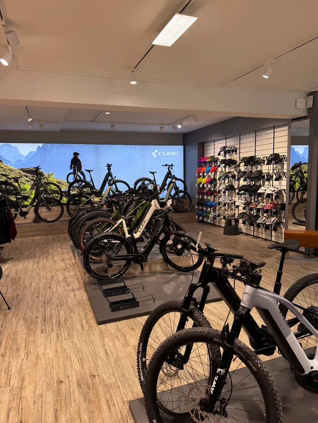 Innenansicht eines Fahrradgeschäfts mit E-Bikes, Reifenständern und Helmen an der Wand.