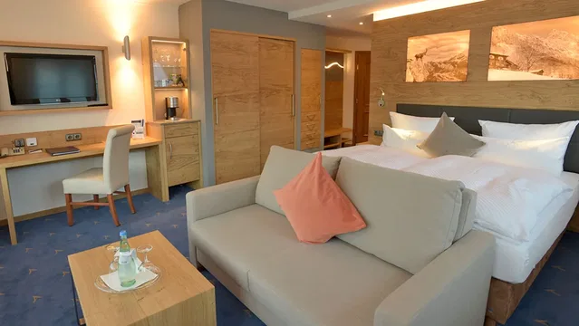 Hotelzimmer mit Bett, Sofa, Schreibtisch und TV im Alpenhof Oberstdorf