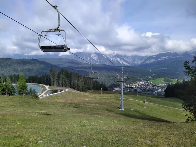 Sesselbahn-Lift führt über grüne Hänge mit Bergpanorama und Dorf im Tal.