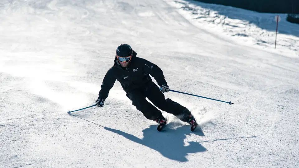 Skifahrer in schwarzer Skiausrüstung beim Kurvenfahren auf einer Piste