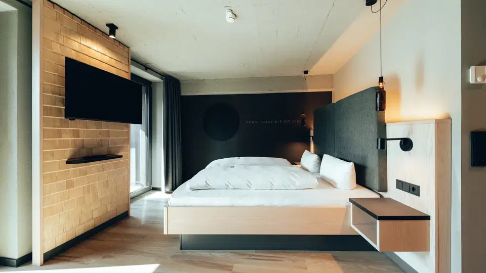 Modernes Hotelzimmer mit Doppelbett, TV an Backsteinwand und Nachttischen