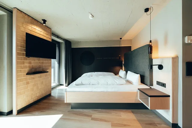Modernes Hotelzimmer mit Doppelbett, TV an Backsteinwand und Nachttischen