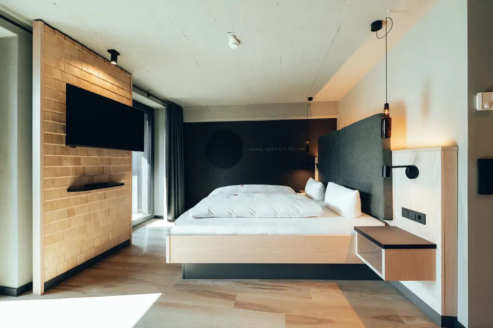 Modernes Hotelzimmer mit Doppelbett, TV an Backsteinwand und Nachttischen
