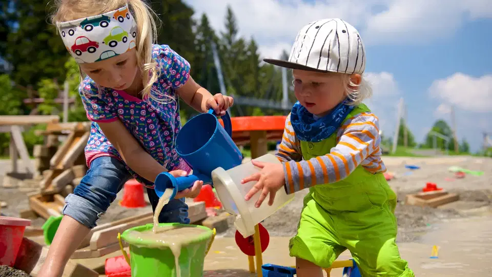 Zwei Kinder spielen mit Wasser und Eimern auf einem Wasserspielplatz.
