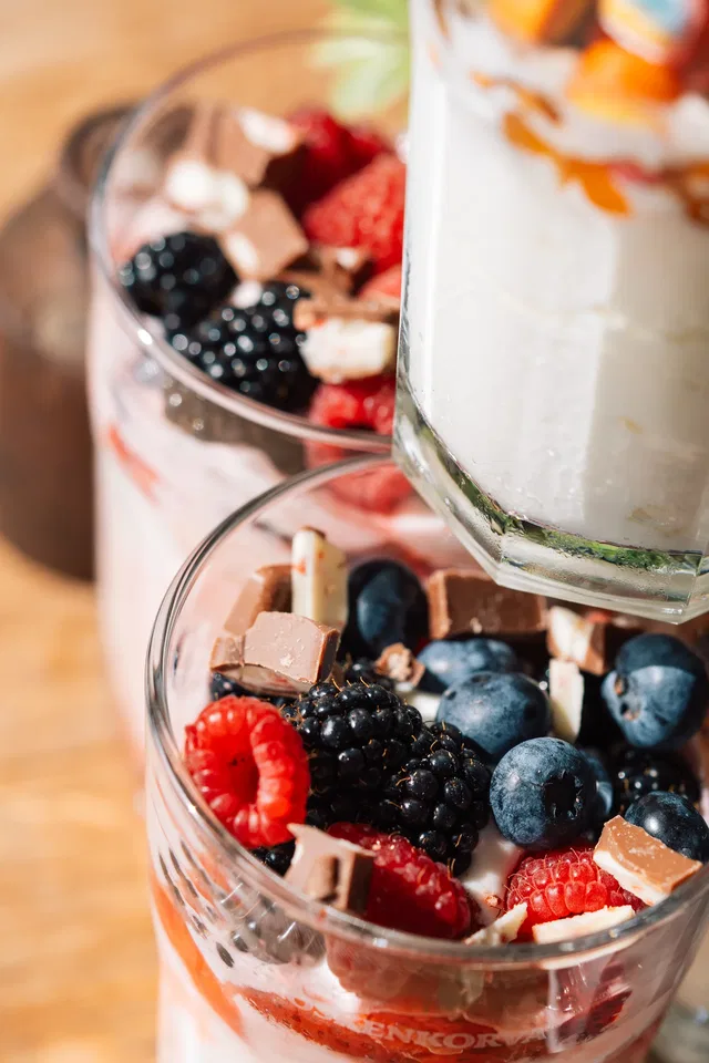 Becher mit Joghurt, Beeren und Schokoladenstückchen neben einem Mixer.