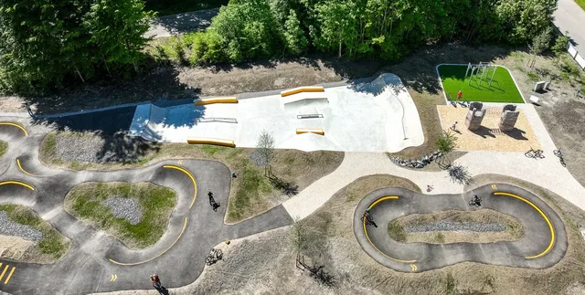 Luftaufnahme eines Skateparks mit Kurvenbahnen, Rampen und Grünflächen.