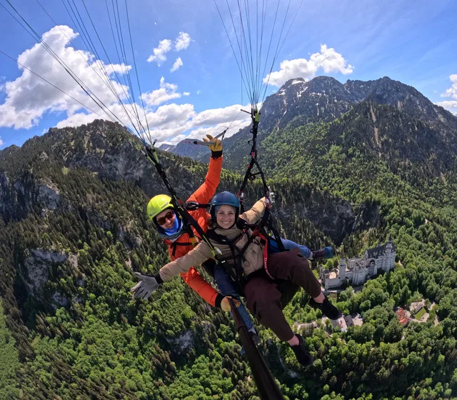 Tandem-Gleitschirmflug vor Schloss Neuschwanstein und Bergkulisse