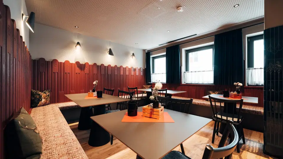 Gastraum mit gepolsterten Sitzbänken, dunklen Holzstühlen und Fensterfront
