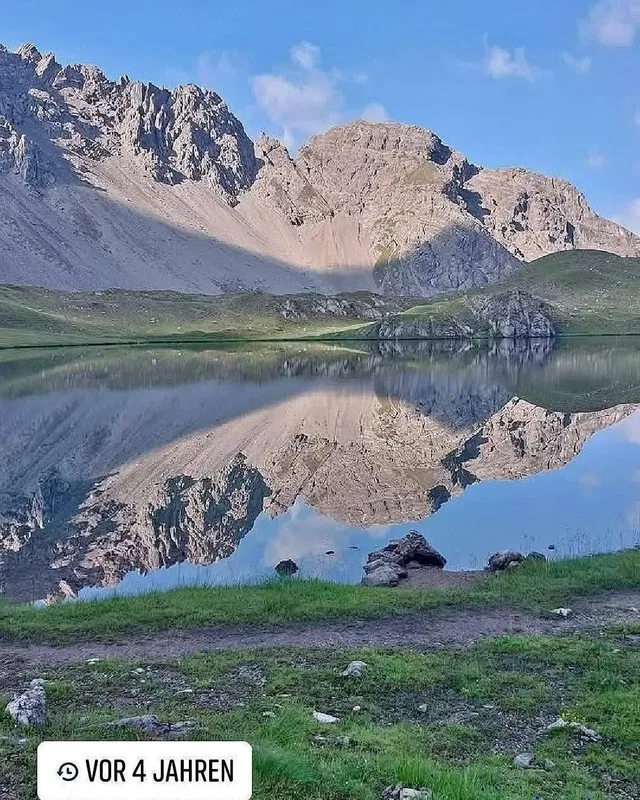 Landschaft mit Bergsee, Spiegelung der Berge im Wasser und grünem Ufer