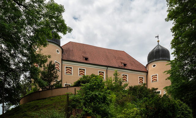 Schloss Kronburg mit runden Türmen hinter einem begrünten Hang