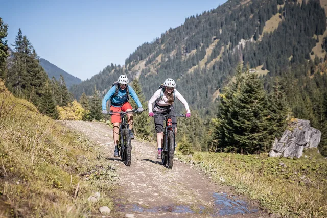 Zwei Mountainbiker auf einem Bergweg vor bewaldeten Berghängen