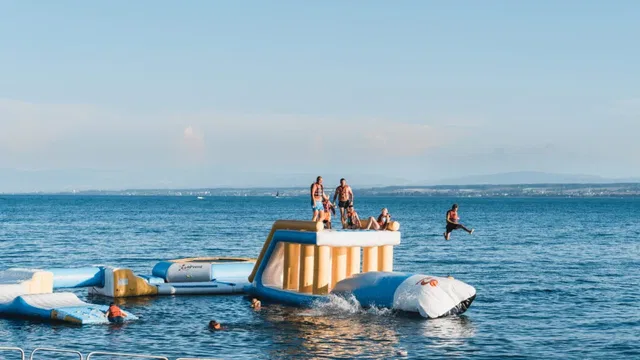Menschen auf einem aufblasbaren Wasserparcours im Meer, einige stehen, andere springen ins Wasser.