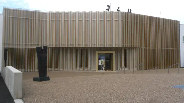 Goldfarbene Lamellenfassade des Museums für zeitgenössische Kunst – Diether Kunerth in Ottobeuren mit Eingang und Skulptur im Vorbereich. Ortsmotiv.