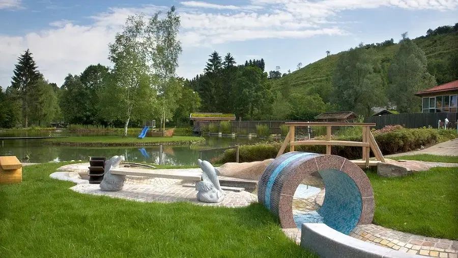 Außenspielbereich am See mit Wasserspiel, ringförmigem Tunnel und Holzkonstruktionen