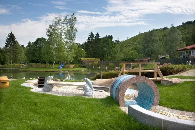Außenspielbereich am See mit Wasserspiel, ringförmigem Tunnel und Holzkonstruktionen