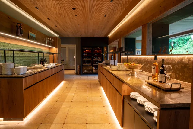 Moderne Buffet-Lounge mit zwei Holztheken, warmem Licht und Teller- sowie Flaschenbereich.