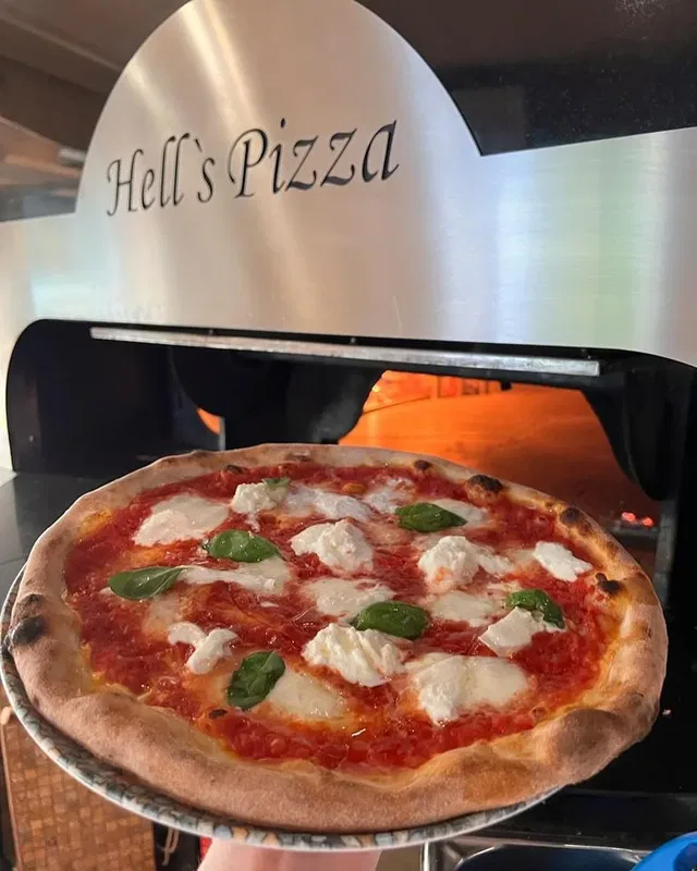 Pizza auf einer Pizzaschaufel vor dem Holzofen von Hell’s Pizza