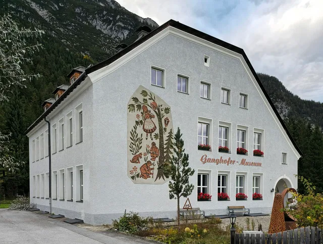 Weißes Museumsgebäude mit Wandfresko und Blumenfenstern am Berg.