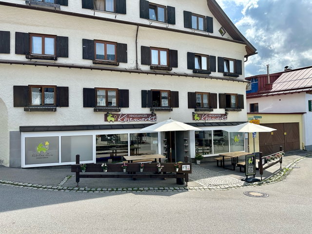 Eingang des Hindelanger Käsemarkts mit Tischen und Sonnenschirmen