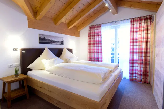 Kuscheliges Schlafzimmer mit Holzbalkendecke, großem Bett und weißen Bettwaren.