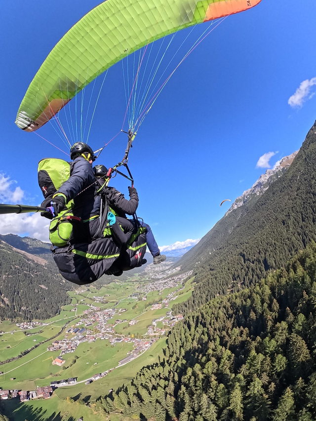 Tandemgleitschirm mit grünem Schirm über einem weiten Alpental
