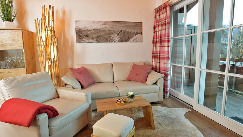 Wohnzimmer der Ferienwohnung Söllereck mit hellem Sofa, Sessel und Zugang zum Balkon.