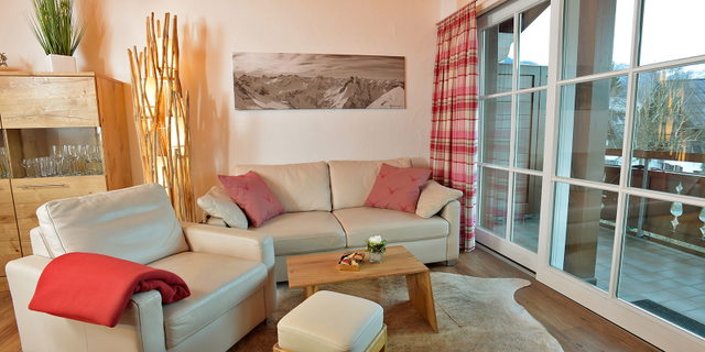 Wohnzimmer der Ferienwohnung Söllereck mit hellem Sofa, Sessel und Zugang zum Balkon.