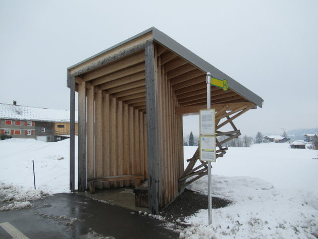 Die hölzerne Architekturhaltestelle Glatzegg in Krumbach vor verschneiter Landschaft.
