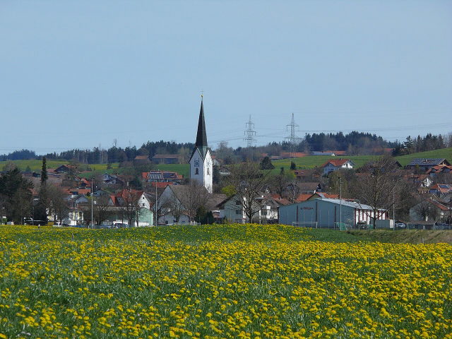 Blick über eine Löwenzahnwiese auf den Ortskern von Durach mit Kirche