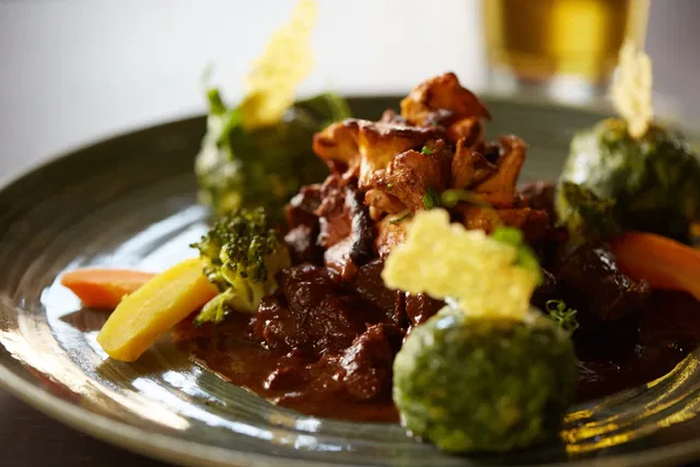 Angerichteter Teller mit dunkler Sauce, Gemüse und knuspriger Garnitur
