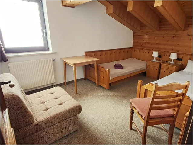 Schlafzimmer im Holzhaus mit zwei Einzelbetten, Sessel, Tisch und Dachboden-Optik