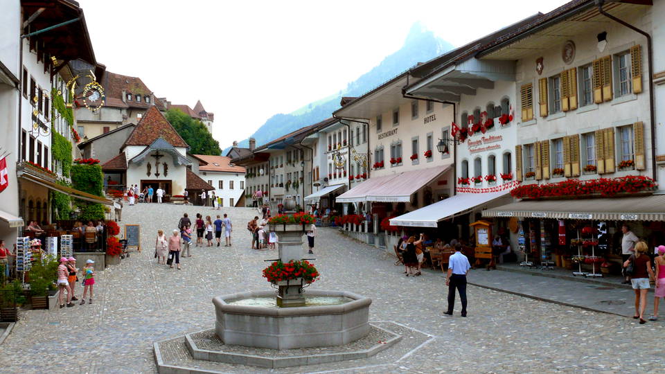 Gepflasterte Hauptgasse von Gruyères mit Brunnen und historischen Häuserzeilen