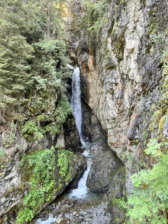 Kantenschlucht mit kleinem Wasserfall zwischen felsigen Wänden und grüner Vegetation.