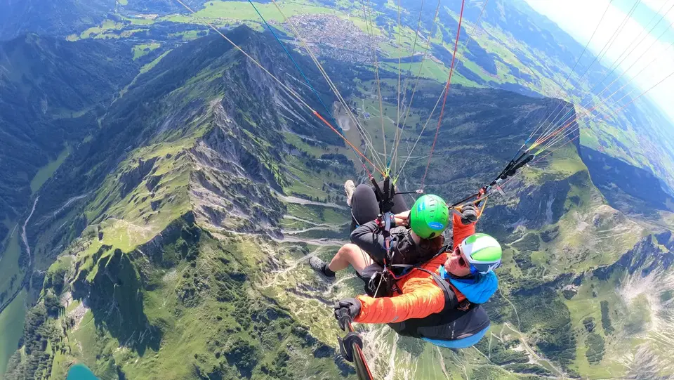 Passagier und Tandempilot über grünen Bergkämmen und einem See