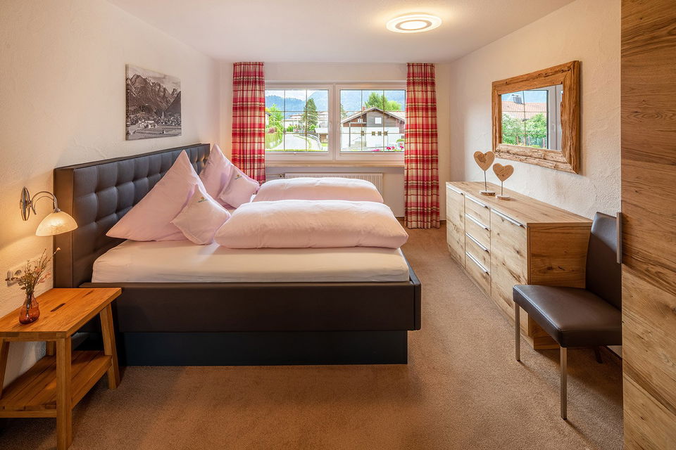 Schlafzimmer der Ferienwohnung Fellhorn mit Doppelbett, Holzkommode und Bergblick.