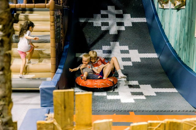 Kinder spielen auf einer gepolsterten Rutsche und Kletterwand.