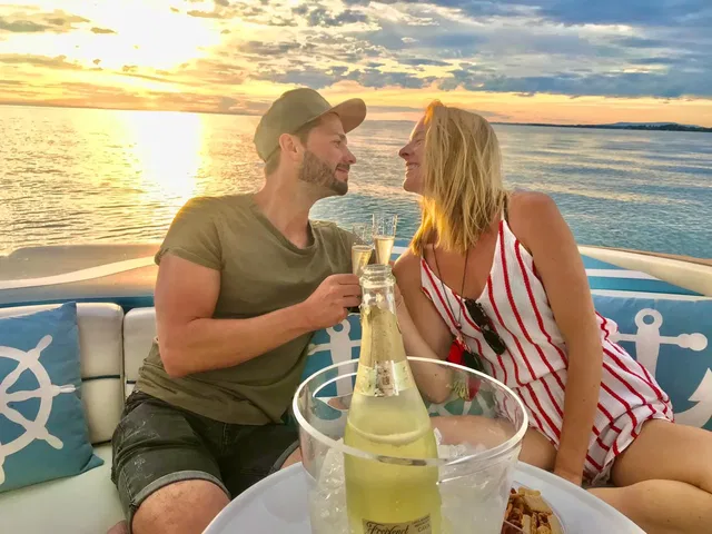 Paar sitzt auf einem Boot bei Sonnenuntergang und stoßt mit Champagner an.