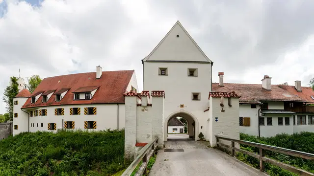 Zugangsbrücke und Torhaus der Mindelburg mit hellen Mauern, roten Dächern und Burggraben. Ortsmotiv zur Ausflugsplanung.