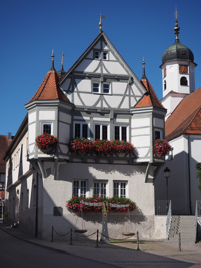 Fachwerkgiebel des Rathauses Hayingen mit Blumen und Kirchturm im Hintergrund