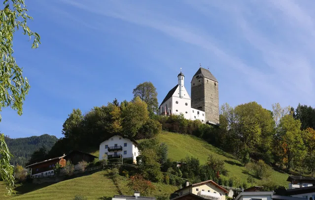 Kirche und steinerner Turm auf einem bewaldeten Hügel über Häusern