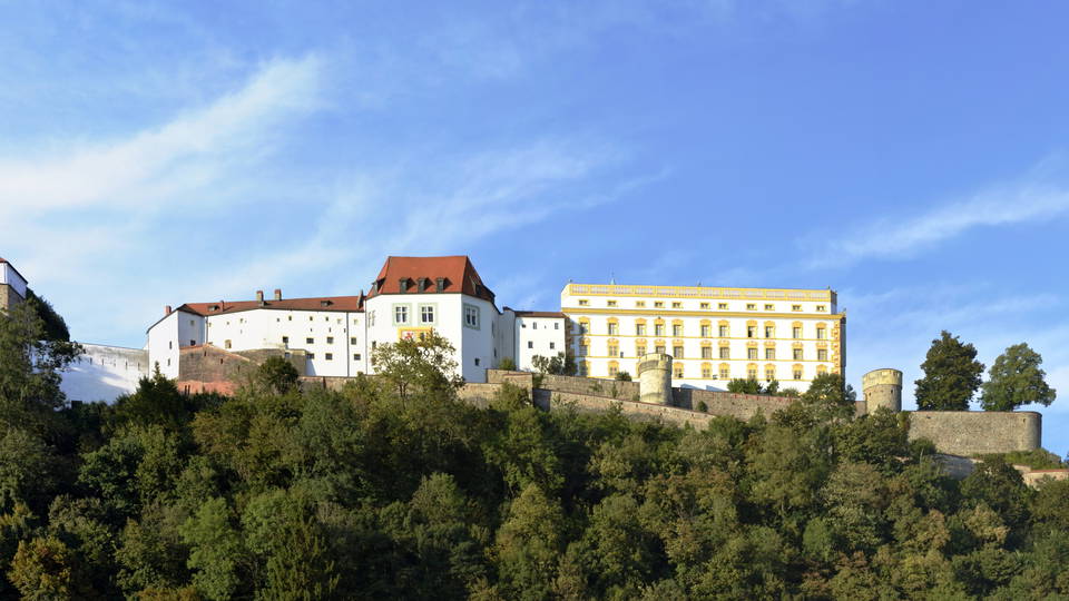 Die Veste Oberhaus in Passau mit ihren Gebäuden und Mauern über dem bewaldeten Hang.
