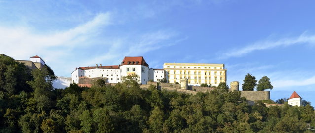 Die Veste Oberhaus in Passau mit ihren Gebäuden und Mauern über dem bewaldeten Hang.