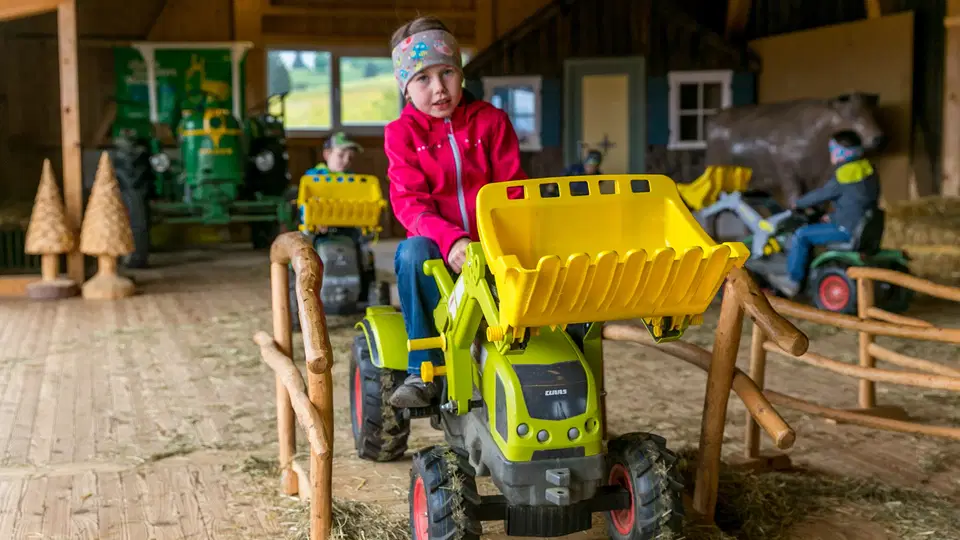 Kind auf einem gelb-grünen Trettraktor im überdachten Parcours
