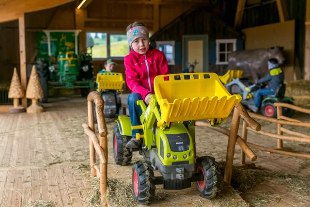 Kind auf einem gelb-grünen Trettraktor im überdachten Parcours