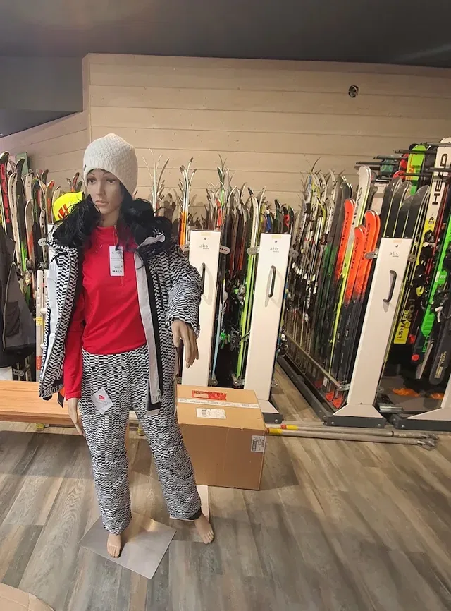 Ski-Shop-Deko-Puppe mit rotem Pullover und gemustertem Outfit vor Skiern.