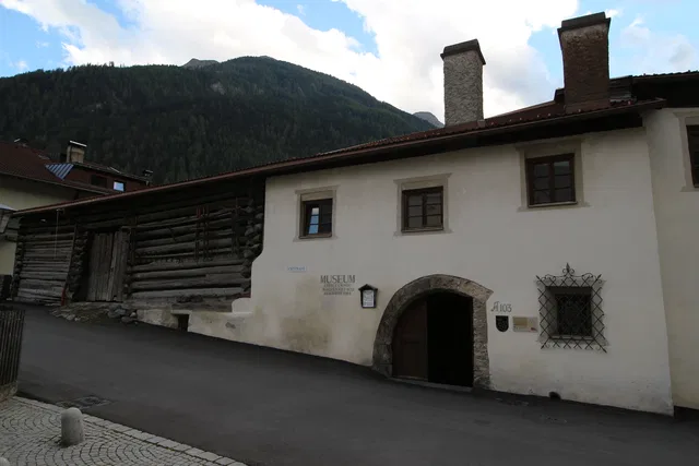 Historisches Gebäude mit Torbogen, Museumszeichen und Fensterfront vor einer Berglandschaft.